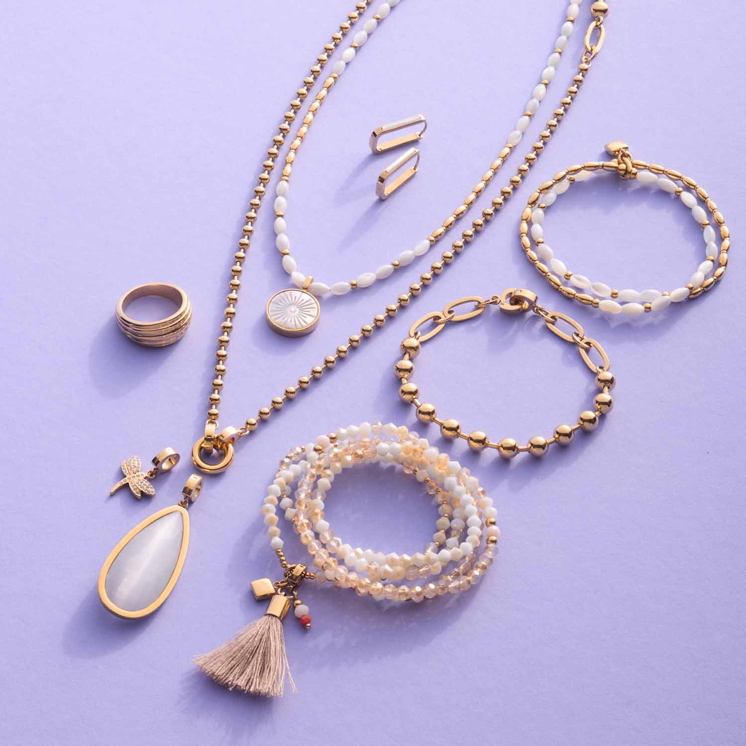 Schmuckkollektion mit Armbändern, Ketten, Ring und Ohrringen in Gold auf violettem Hintergrund
