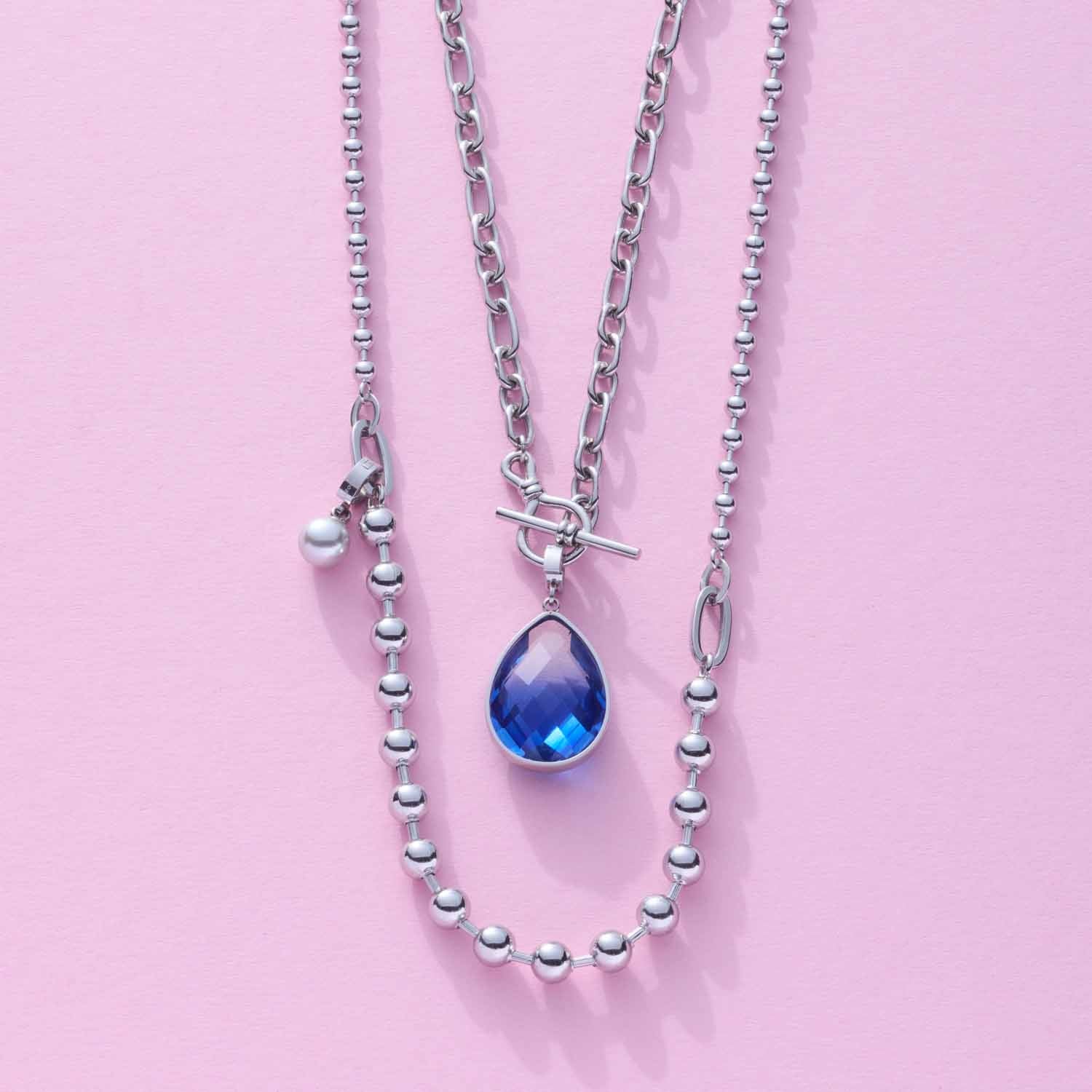 Halskette ELISABETH mit silbernen Kugelketten und blauem Tropfenanhänger auf rosa Hintergrund