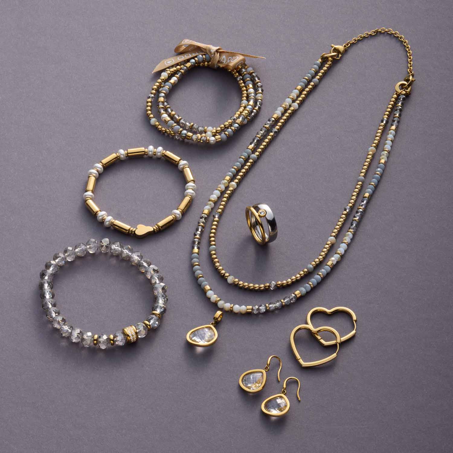 BERNA Schmuckkollektion mit Armbändern, Kette und Ring auf grauem Hintergrund