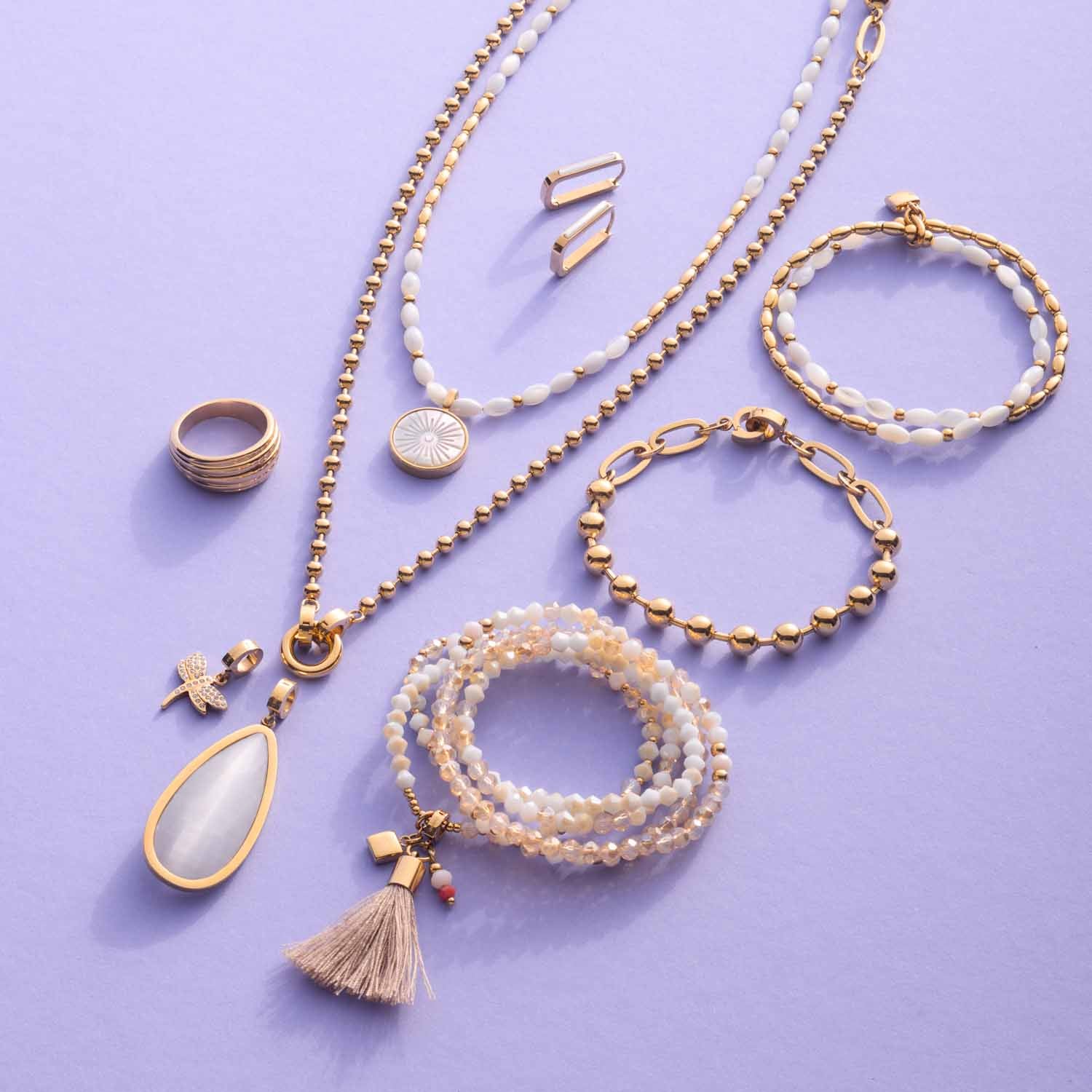 Schmuckkollektion mit Halsketten, Armbändern, Ring und Ohrsteckern in Gold und Perltönen auf lila Hintergrund