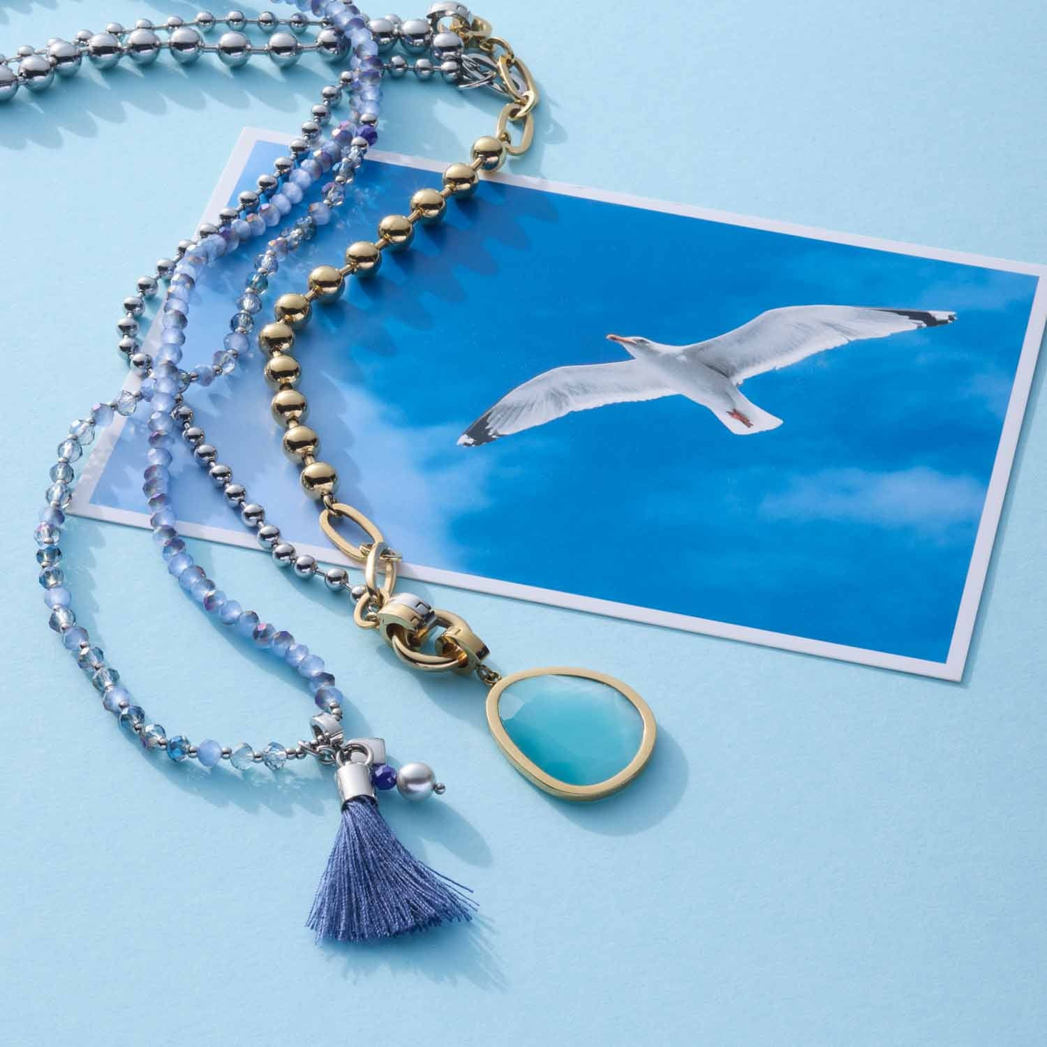 Halskette DONNA blau mit Glasperlen, Quaste und Türkis-Anhänger auf blauem Untergrund neben Walmotiv-Fotografie