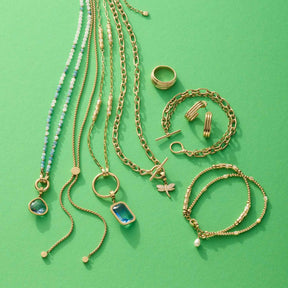 Schmuckkollektion mit goldenen Ketten, Armbändern, Ring und Ohrringen auf grünem Hintergrund