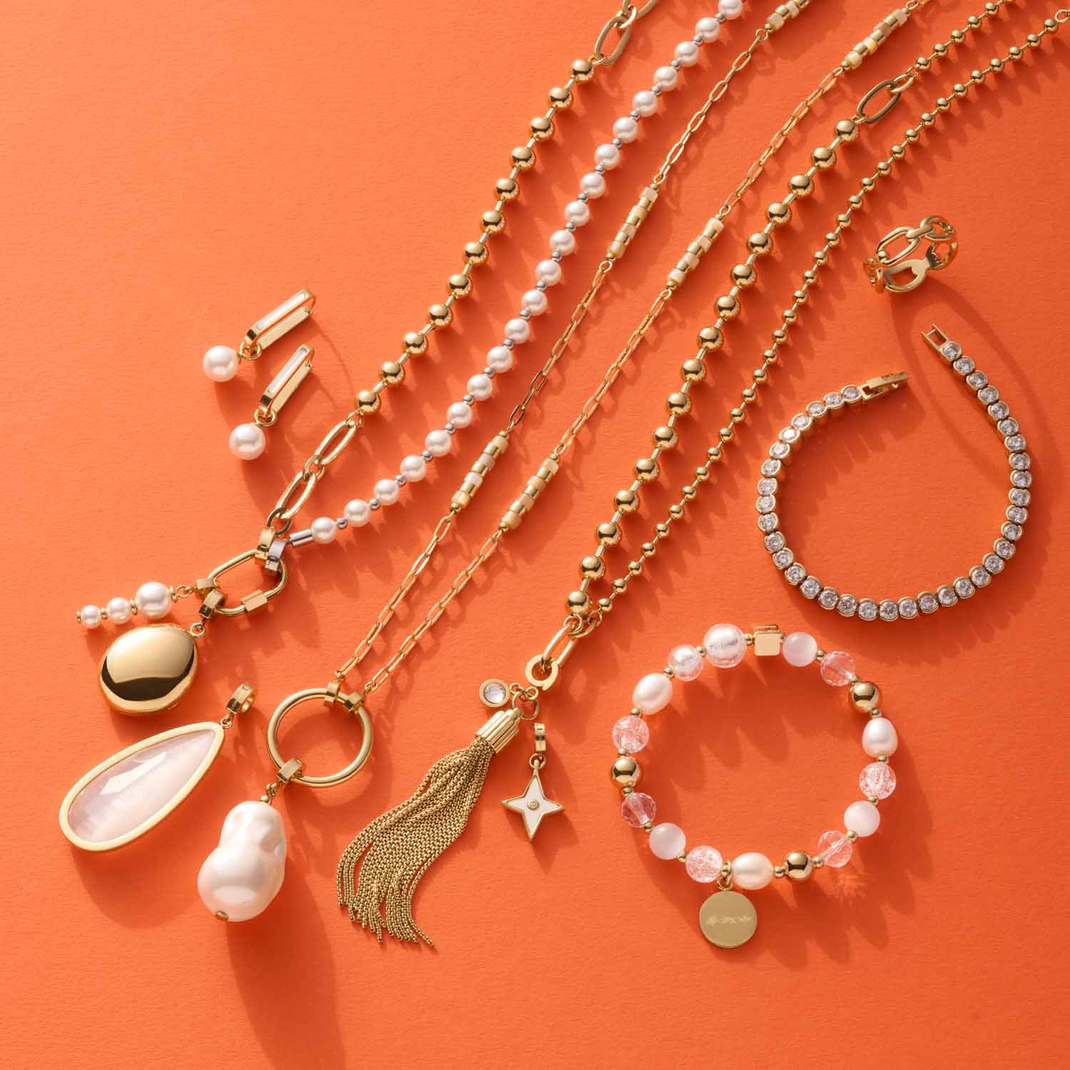 Schmuckkollektion mit Ketten, Anhängern, Armbändern und Ohrringen auf orangefarbenem Hintergrund