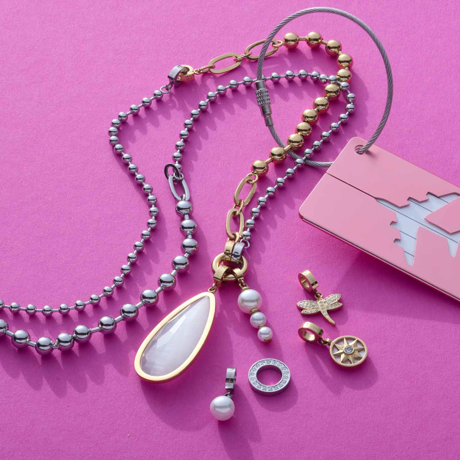 Anhänger JESSY gold Clip & Mix mit verschiedenen austauschbaren Charms auf rosa Hintergrund