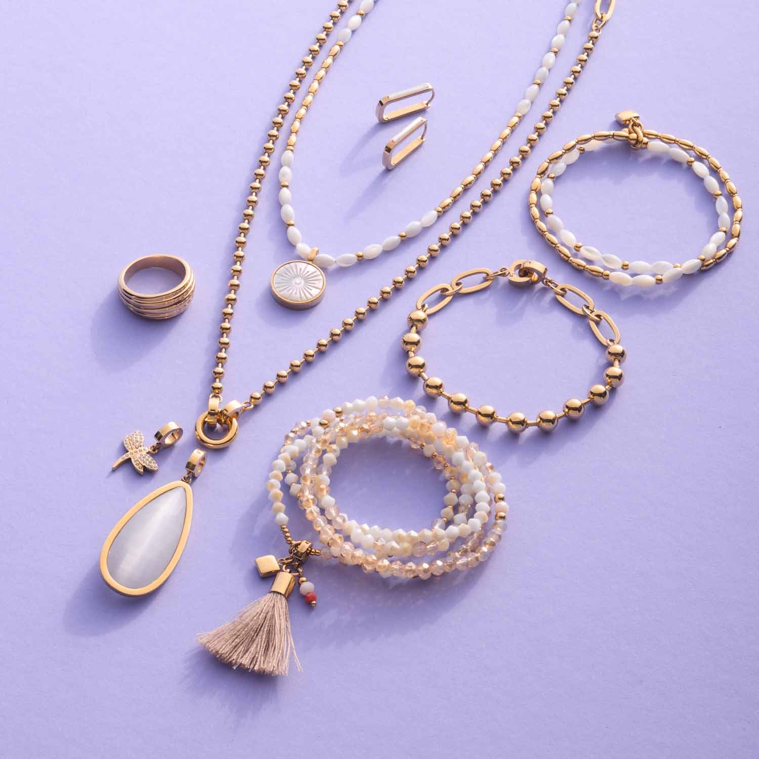 Goldener Schmuck mit Anhängern, Ringen, Ketten und Armbändern auf violettem Hintergrund