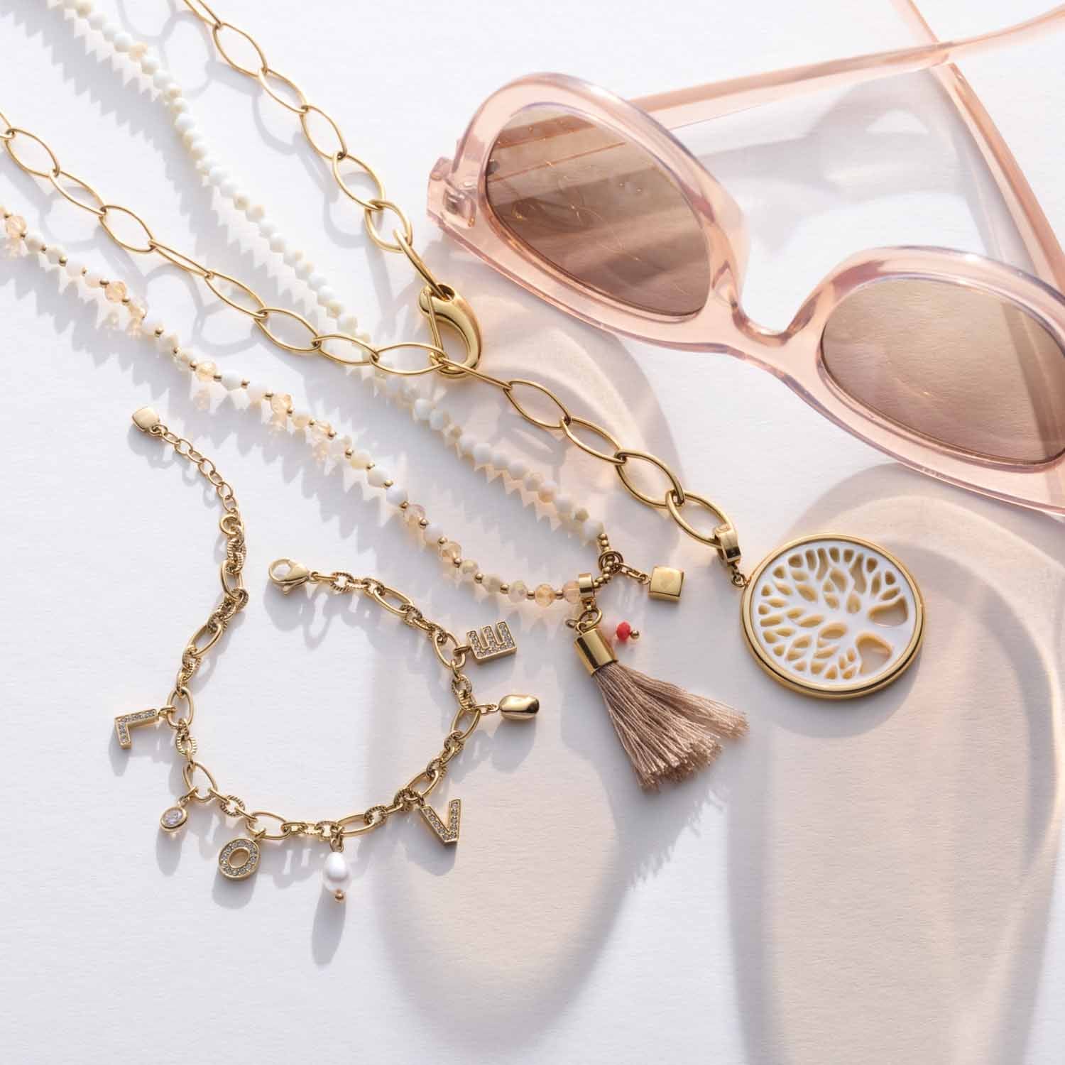 Anhänger TREENA gold mit Muscheldetail, Schmuckketten und rosafarbener Sonnenbrille auf weißem Hintergrund