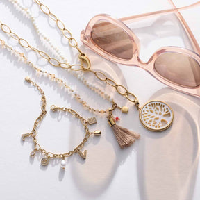 Anhänger TREENA gold mit Muscheldetail, Schmuckketten und rosafarbener Sonnenbrille auf weißem Hintergrund