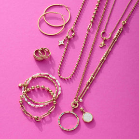 Goldener Schmuck arrangiert auf rosa Untergrund: Ohrringe, Ringe, Ketten und Anhänger CLARENCE gold Clip & Mix