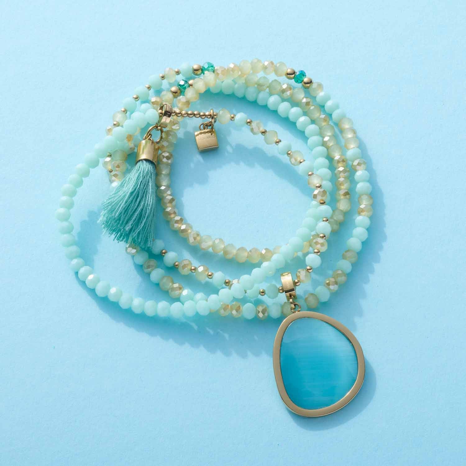 Anhänger BONNY gold Clip & Mix mit Perlenkette und Quaste auf blauem Hintergrund