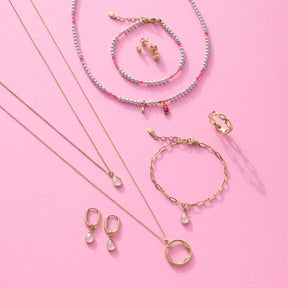 Schmuck-Kollektion mit Halsketten, Armbändern, Ringen und Ohrringen in Gold auf rosa Hintergrund
