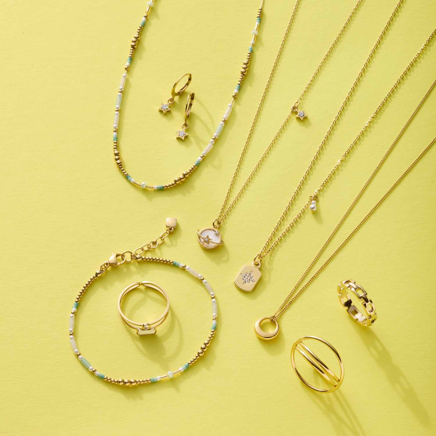 Armband LILLY gold CIAO mit Glas-Perlen auf gelbem Hintergrund, umgeben von weiteren Schmuckstücken der Serie