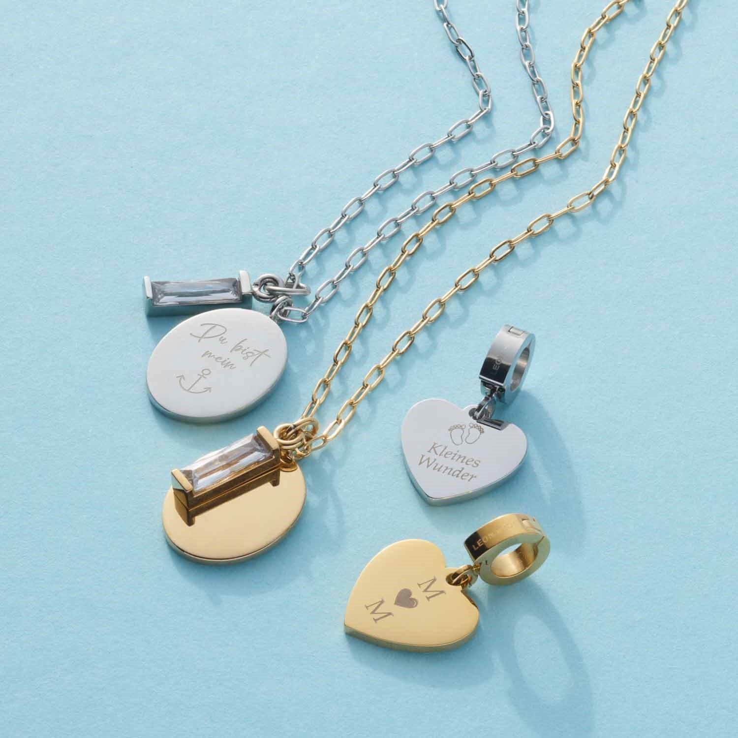 Vier gravierte Halsketten in Silber und Gold auf hellblauem Hintergrund mit personalisierten Anhängern