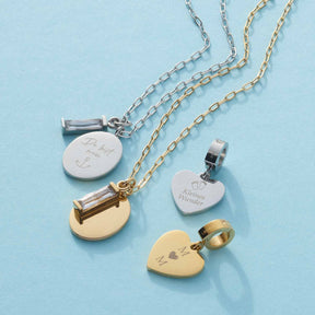 Vier gravierte Halsketten in Silber und Gold auf hellblauem Hintergrund mit personalisierten Anhängern