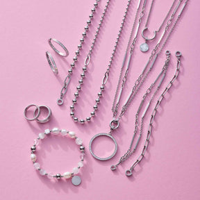 Silberner Schmuck auf rosa Hintergrund: Ringe, Ketten und Armbänder aus Edelstahl