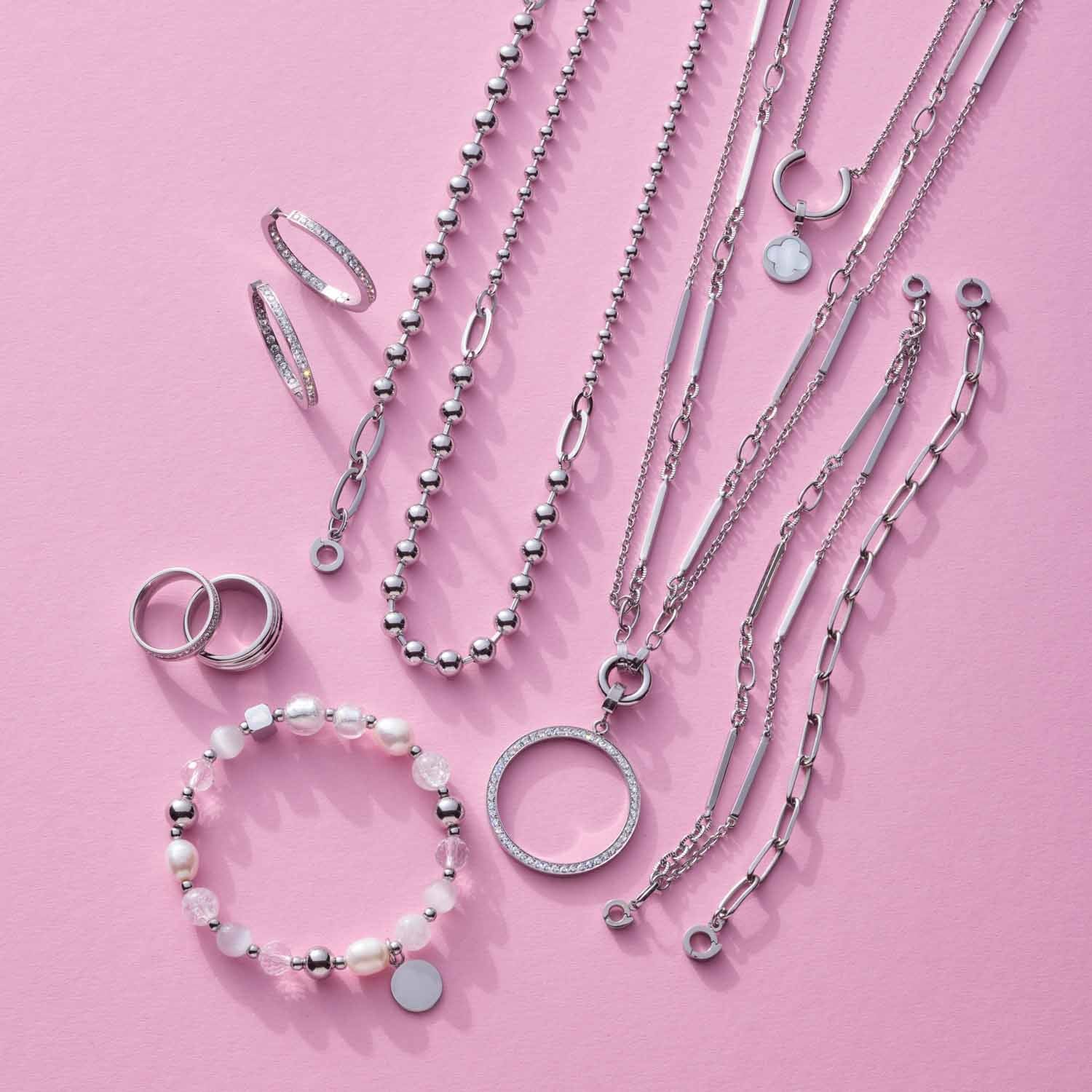 Silberne Schmuckkollektion auf rosa Hintergrund: Ringe, Ketten und Armband aus Edelstahl