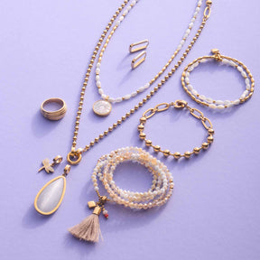 Goldener Schmuck auf lilafarbenem Hintergrund, darunter Ringe, Ketten, Armbänder und Ohrringe