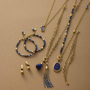 Schmuckkollektion mit Halsketten, Armbändern und Ohrringen in Gold mit blauen Glasperlen auf beigem Hintergrund