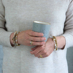 Frau traegt Armband NINA gold an Handgelenk, haelt Keramiktasse