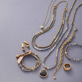Halskette CATHERINE mit Perlen, Ringen und Anhängern auf grauem Hintergrund