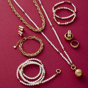Schmuckkollektion mit goldenen Ketten, Perlenarmbaendern, Ringen und Ohrringen auf pink-rotem Hintergrund