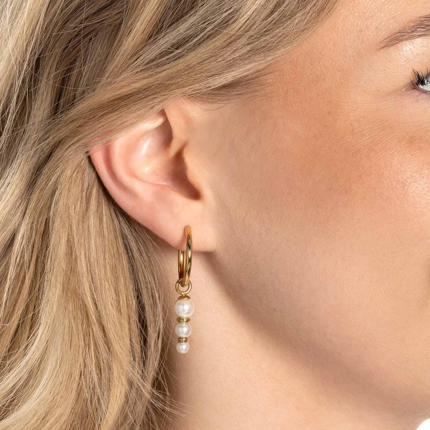Frau traegt goldene Ohrringe JUSTINE mit weissen Perlenhaengern
