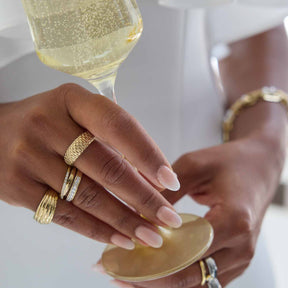 Frau mit goldenen Ringen an Sektglas, Nahaufnahme Hand