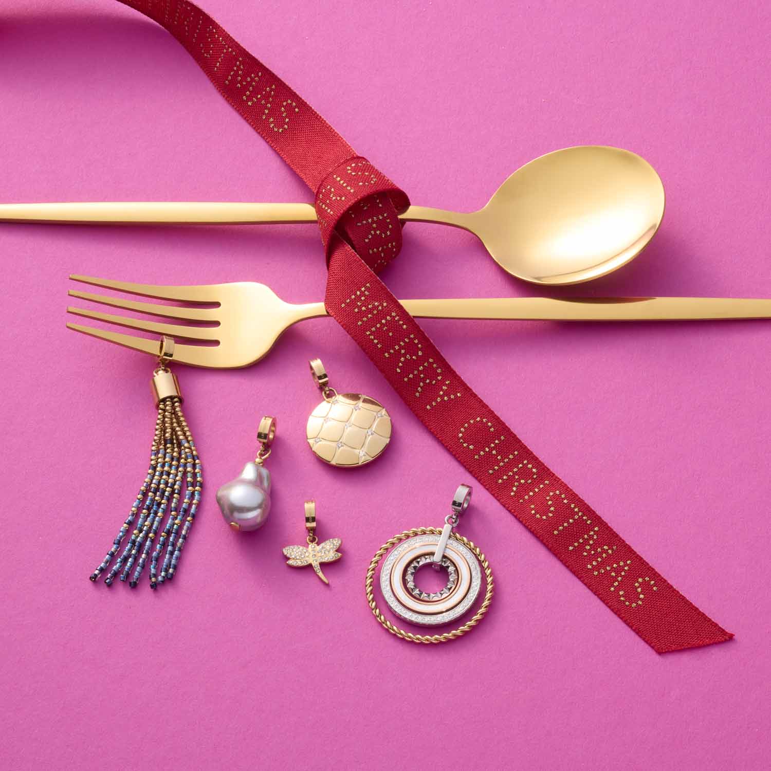 Goldbesteck und bunte Schmuckanhänger auf rosa Hintergrund mit rotem Band