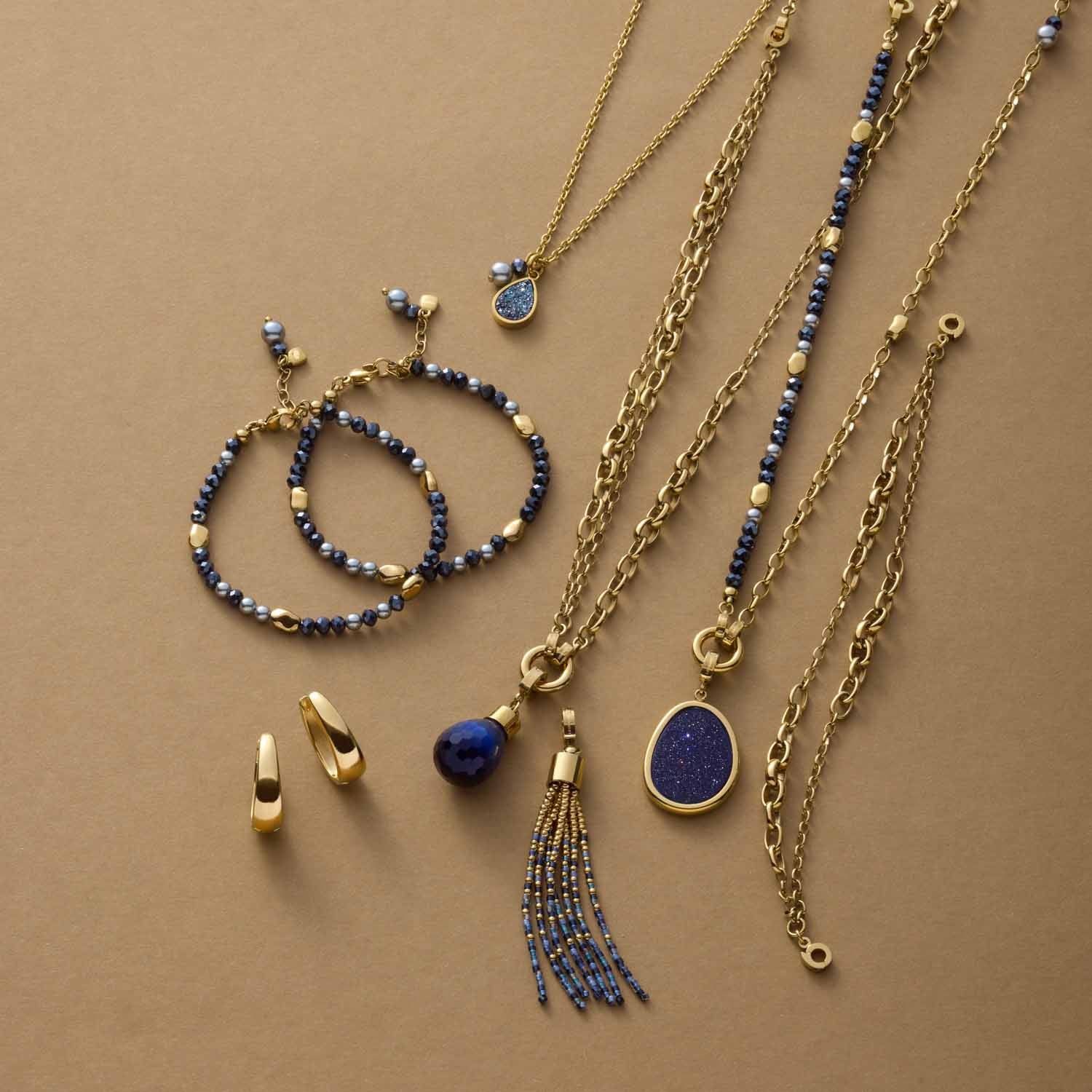 Schmuckset mit Anhängern, Ketten und Armbändern in Gold und Blau auf beigem Untergrund