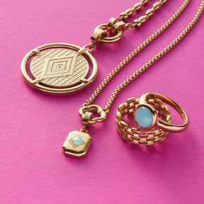 Goldener Schmuck mit Anhängern und Ring auf rosa Hintergrund