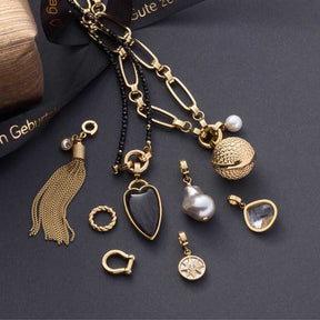 Verschiedene goldene Schmuckcharms und Anhaenger auf grauem Untergrund, darunter Herzform, Perlen und Kettenelemente