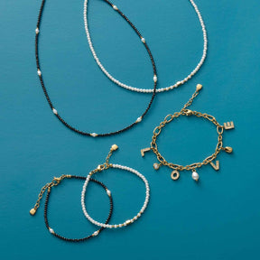 Halsketten und Armbänder aus Glasperlen in Schwarz, Weiß und Gold auf türkisblauem Hintergrund