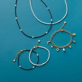 Armbänder und Halsketten aus Glasperlen in Schwarz, Weiß und Gold auf türkisblauem Hintergrund