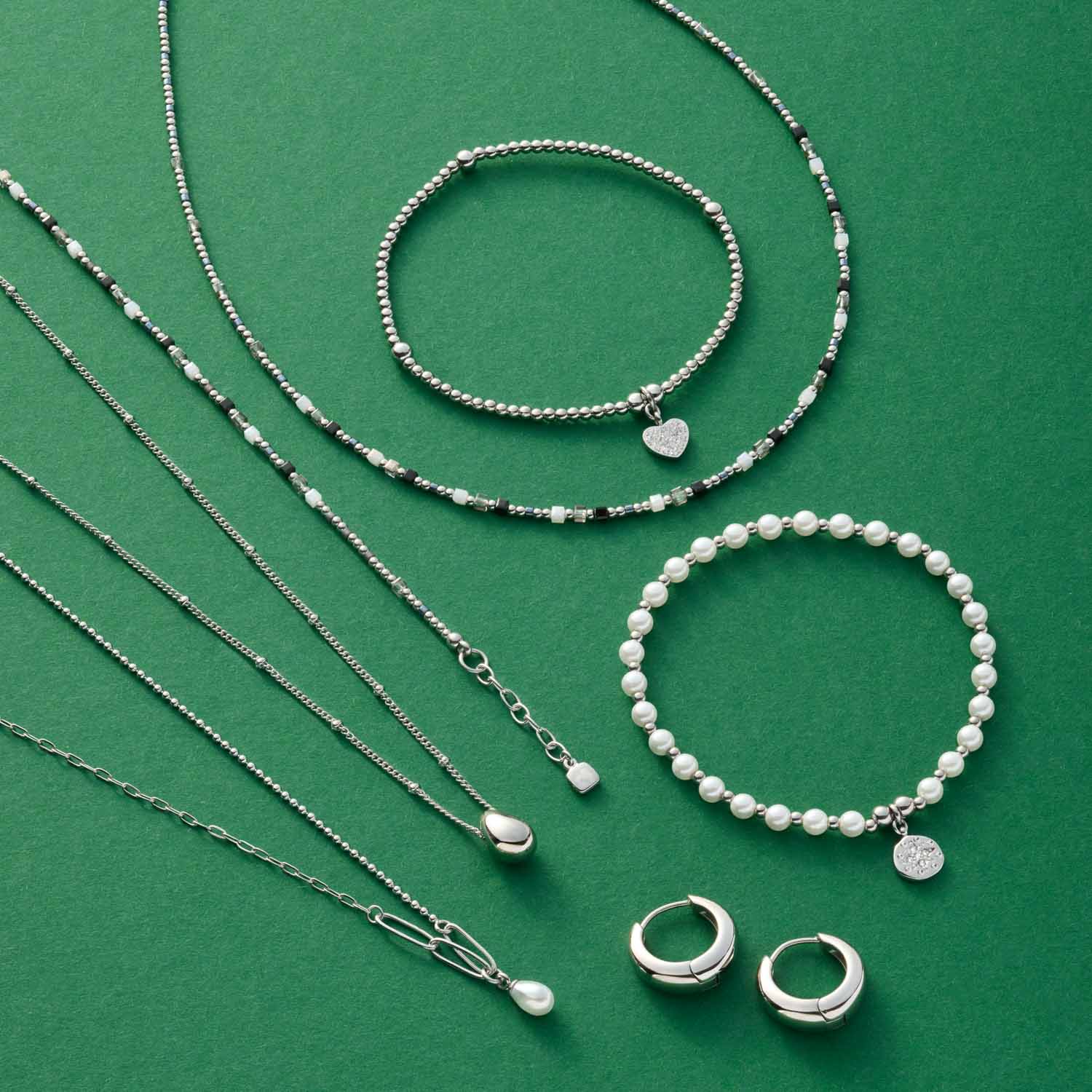 Silberschmuck und Perlenschmuck auf grünem Untergrund: Halsketten, Armbänder und Ringe