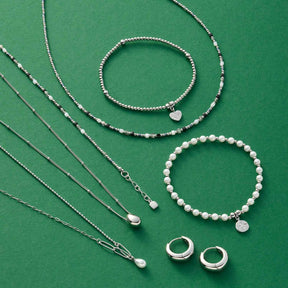 Silberschmuck und Perlenschmuck auf grünem Untergrund: Halsketten, Armbänder und Ringe