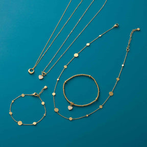 Halskette NOEMI und Armbänder aus der Serie CIAO in Gold auf blauem Hintergrund