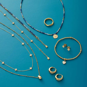Goldene Halsketten, Ringe und Armbänder auf türkisblauem Hintergrund arrangiert