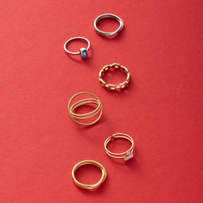 Sechs Ringe aus Silber und Gold auf rotem Hintergrund arrangiert