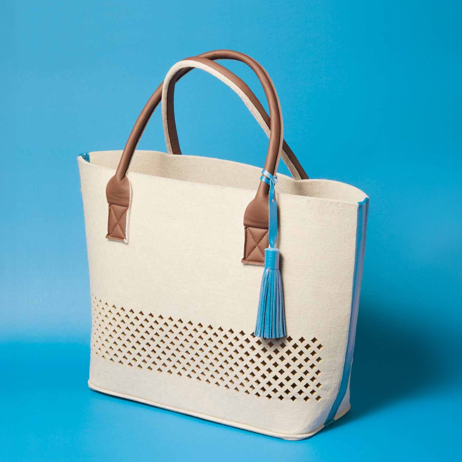 LEONARDO Beach Bag blau in Beige mit braunen Henkeln und blauem Troddel auf blauem Hintergrund