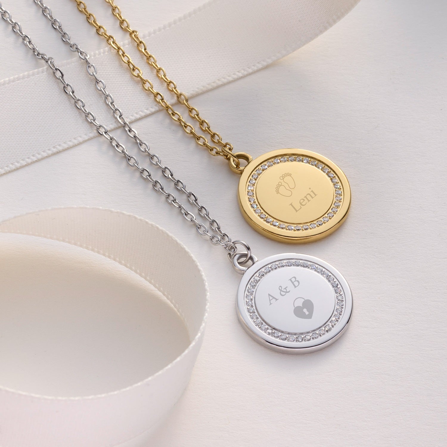 Zwei Halsketten FERRARA mit runden Gravur-Anhängern in Gold und Silber auf weißem Textil
