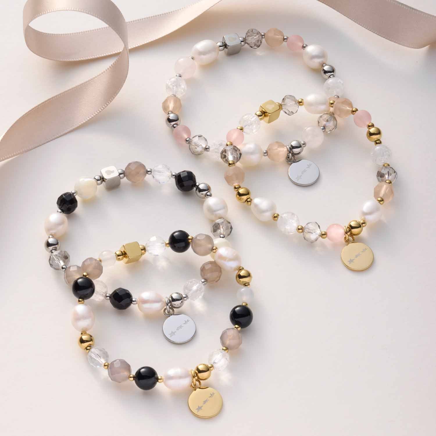 Drei Armbänder HOPE gold/grau mit Perlen und Anhängern auf weißem Hintergrund
