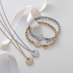 Armband SUE AMOUR gold mit Perlen und Anhängern auf weißem Hintergrund mit Bändern