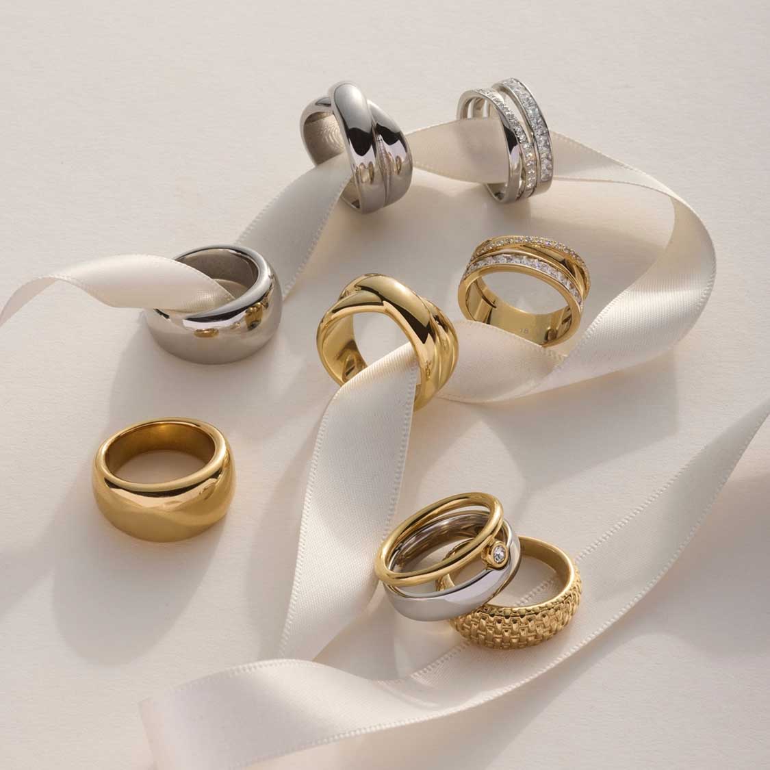 Mehrere Ringe in Gold- und Silbertönen auf weißem Seidenband arrangiert