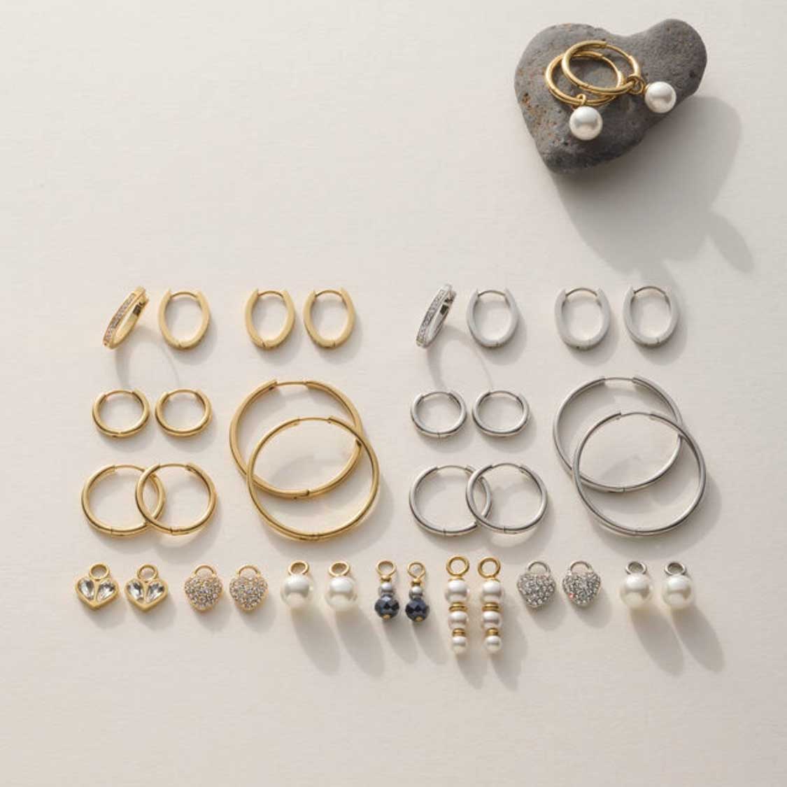 Umfangreiche Schmuckkollektion mit goldenen und silbernen Ringen, Ohrringen und Perlenanhängern auf weißem Untergrund