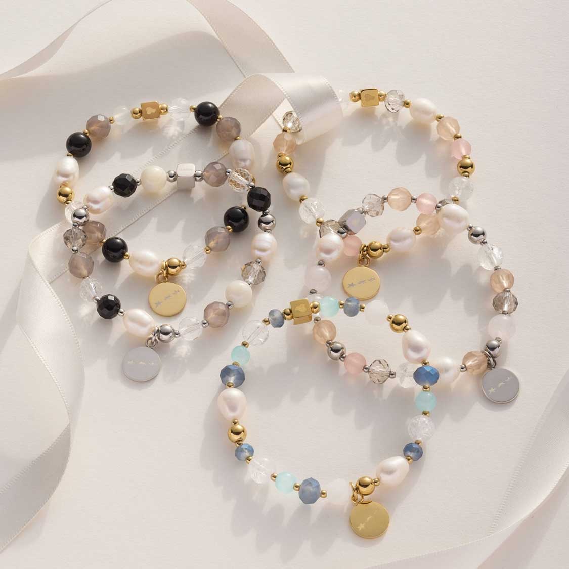 Mehrere Armbänder der Serie HOPE mit Perlen, Glasperlen und goldenen Elementen auf weißem Untergrund