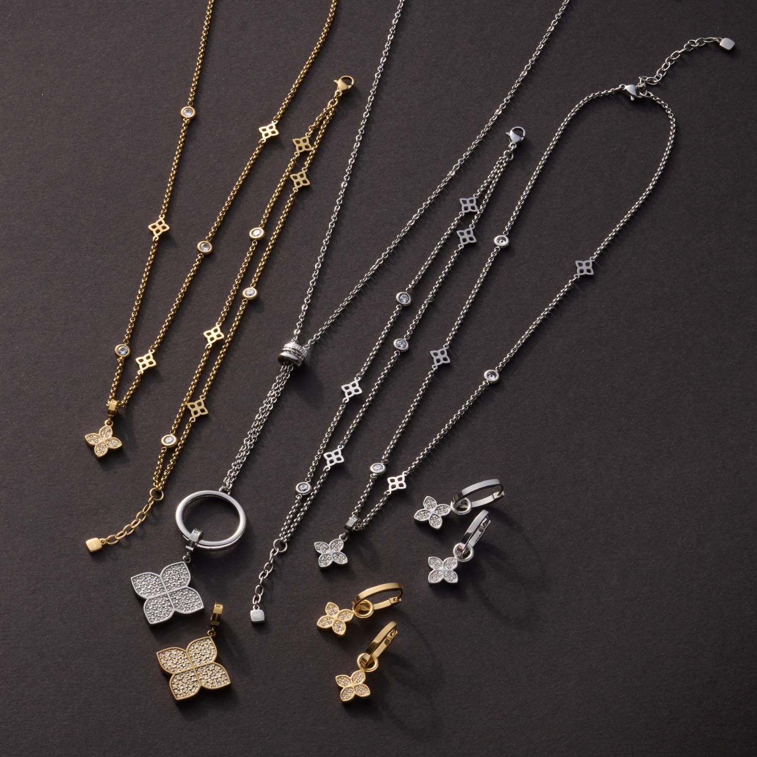 Schmuckkollektion mit Halsketten, Ringen und Ohrringen in Gold und Silber auf grauem Untergrund