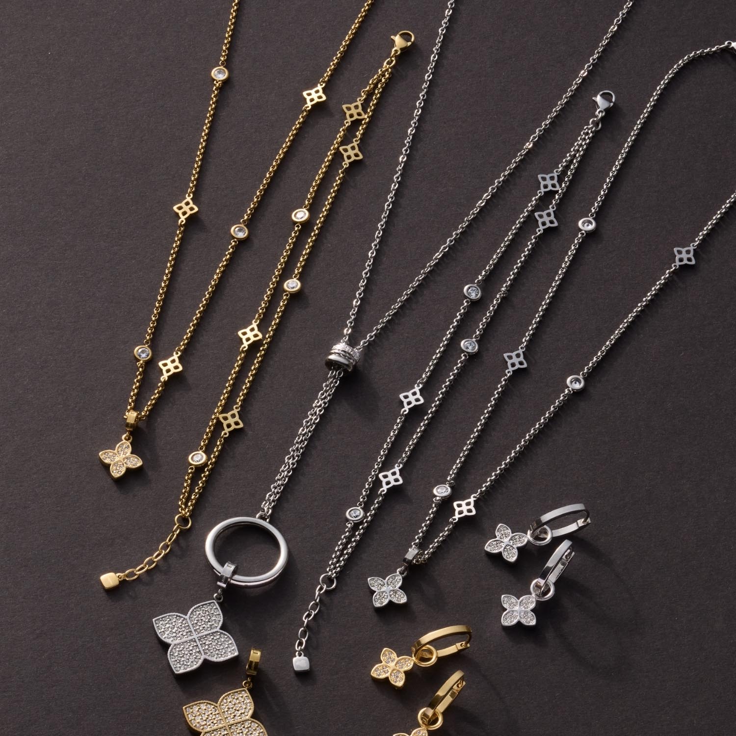 Mehrere Halsketten und Armbänder in Gold und Silber mit Blüten- und Kettendetails auf grauem Hintergrund