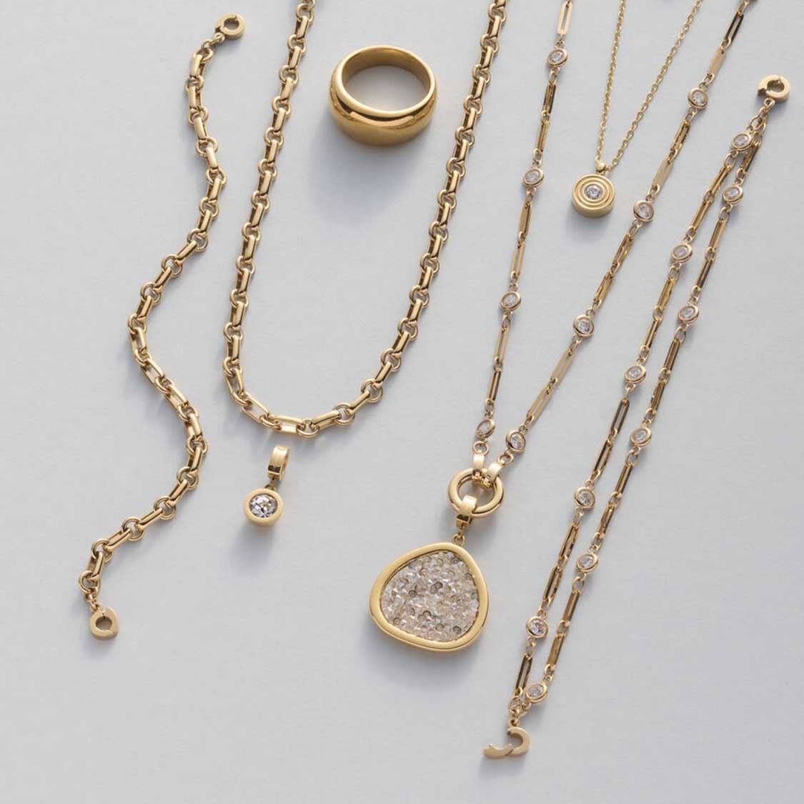 Halskette REBECCA in gold mit verschiedenen Kettengliedern, Ring und Anhängern auf grauem Untergrund