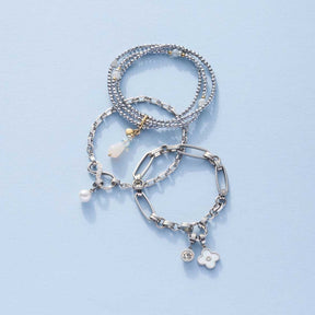 Drei silberne Armbänder YVETTE mit Perlen und Charms auf hellblauem Hintergrund