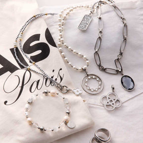 Mehrere Silberschmuck-Ketten und Anhänger BLEUR Clip & Mix auf Papier mit Paris-Motiv arrangiert