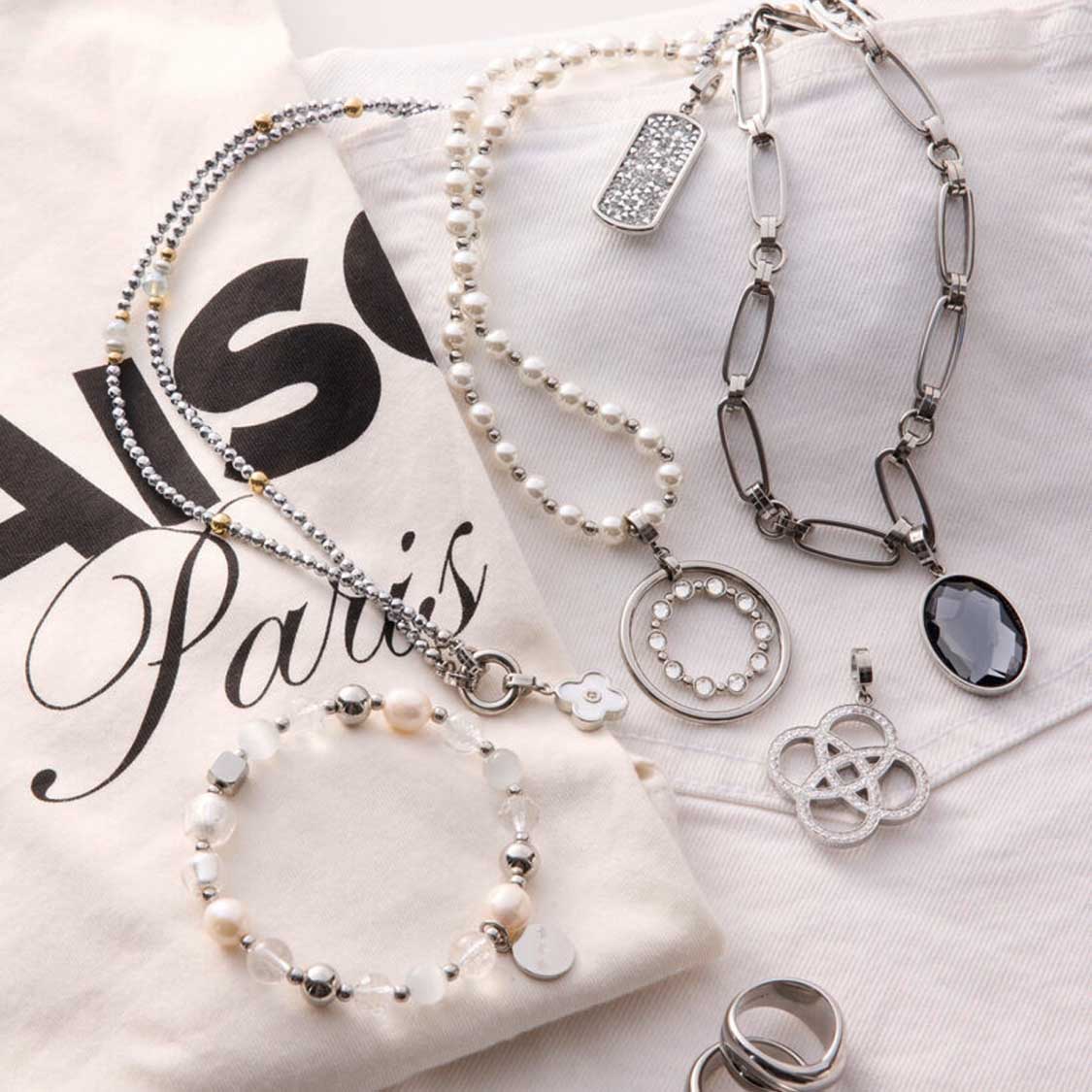 Verschiedene Schmuckketten und Anhänger BLUNA Clip & Mix auf weißem Tuch mit Paris-Schriftzug